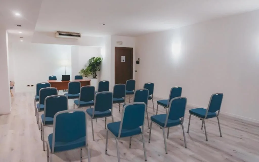 Sala meeting con sedie blu disposte a platea e scrivania