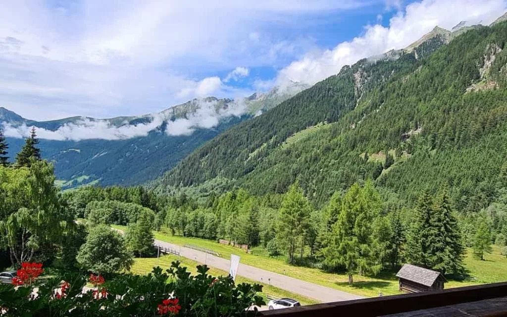 Panorama estivo di una valle alpina verde con boschi e nuvole tra le montagne