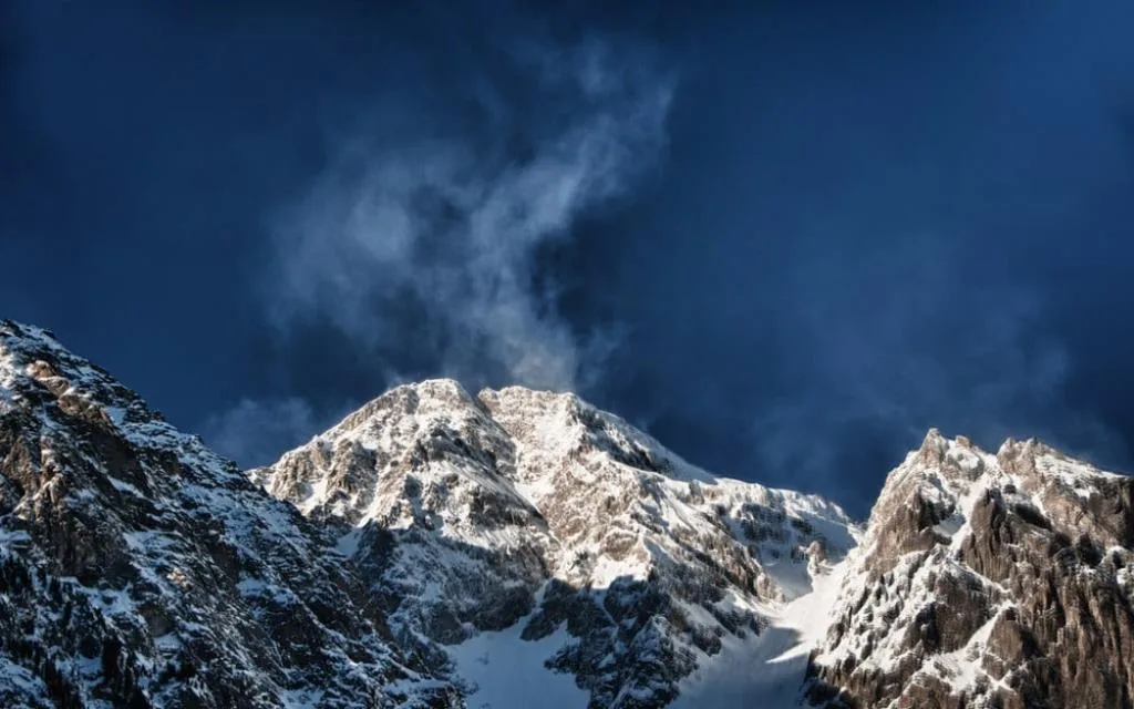 Vetta di montagna innevata con nubi scure sullo sfondo di un cielo blu intenso