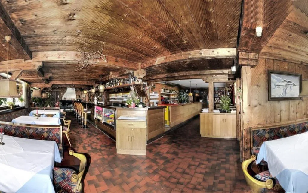 Sala ristorante rustica con soffitto e pareti in legno, bancone bar e tavoli apparecchiati