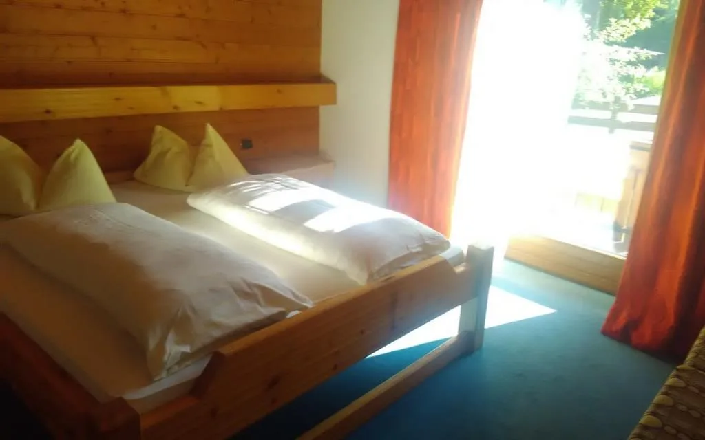 Camera con letto in legno, cuscini gialli e porta finestra con tende rosse