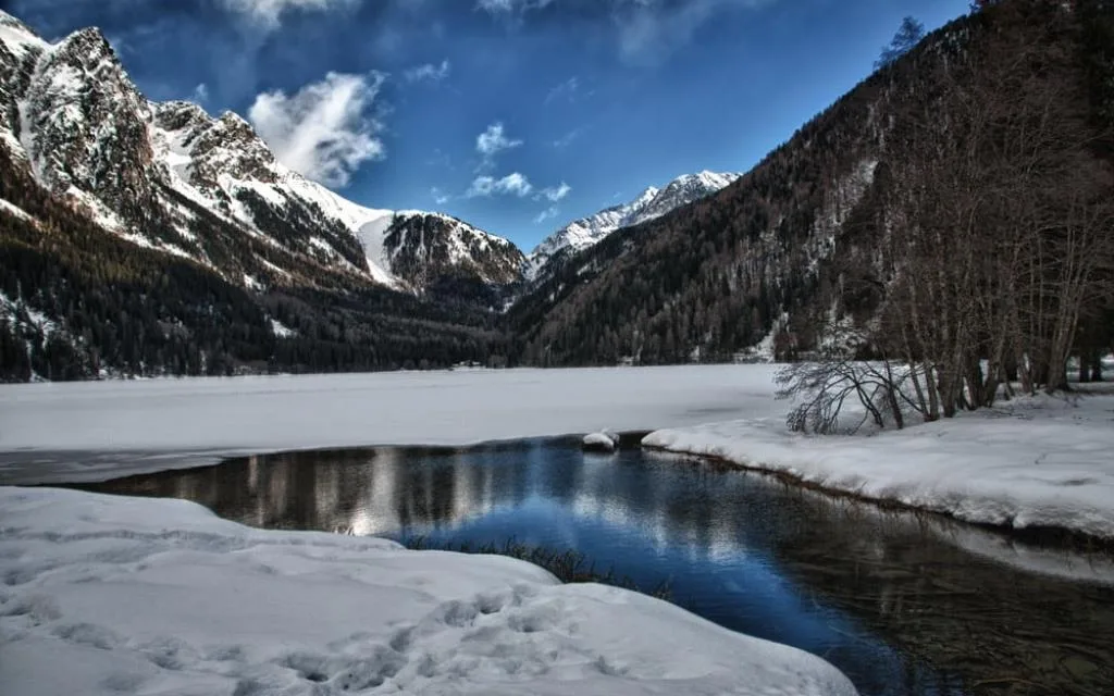 Lago di montagna ghiacciato con neve e riflessi delle cime innevate in inverno