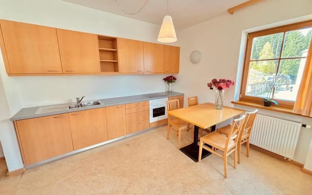 Cucina con mobili in legno, tavolo da pranzo e finestra con vista sul giardino