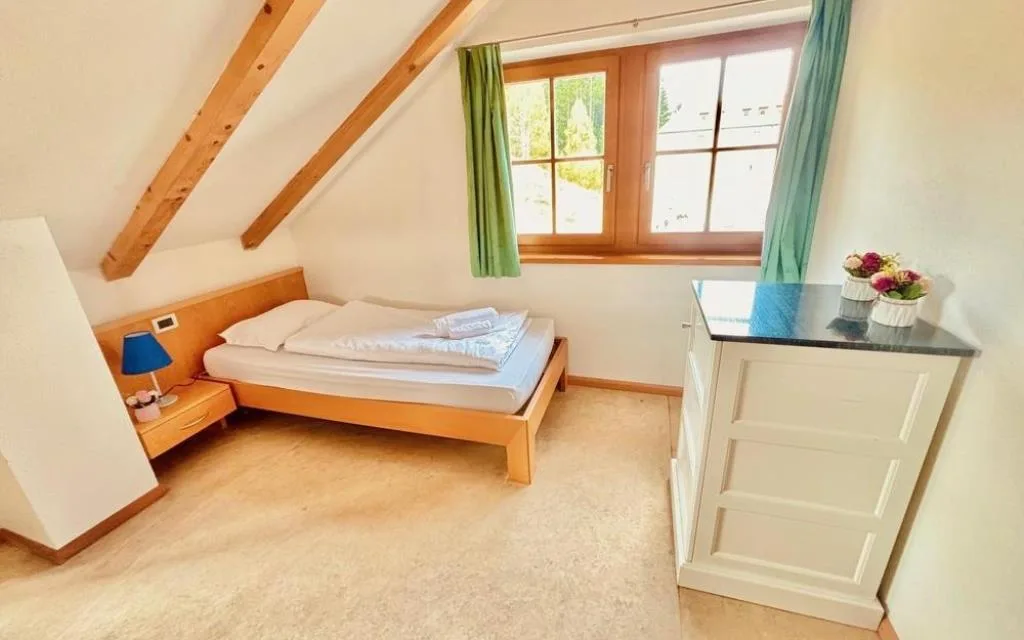 Camera mansardata con letto matrimoniale, travi in legno e finestra con tende verdi
