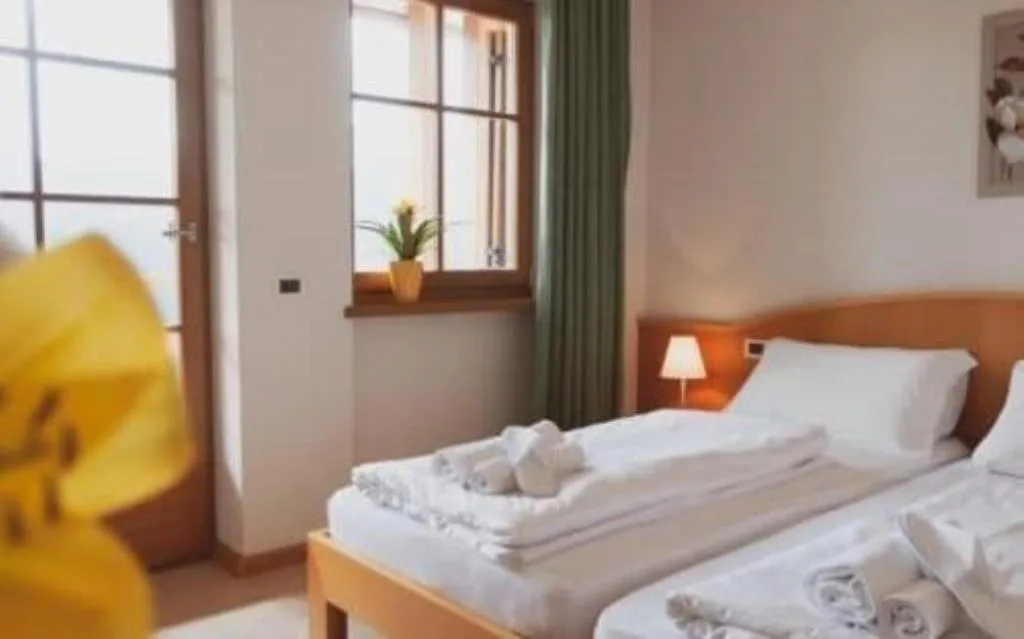 Camera doppia con letto matrimoniale, tende verdi e fiori sul davanzale