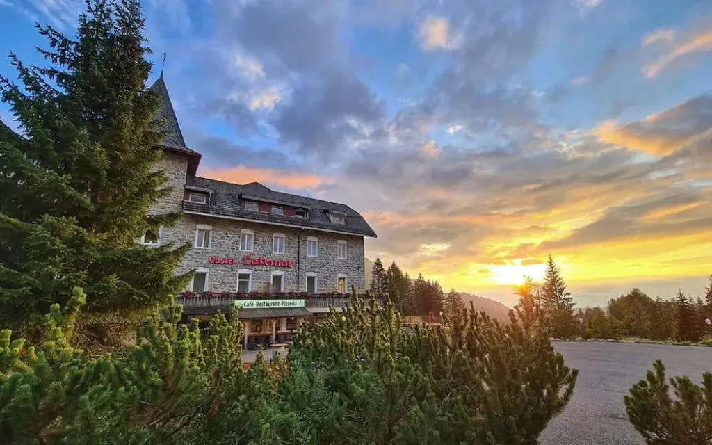 Vista dell'hotel Castel Latemar al tramonto con cielo colorato e alberi in primo piano