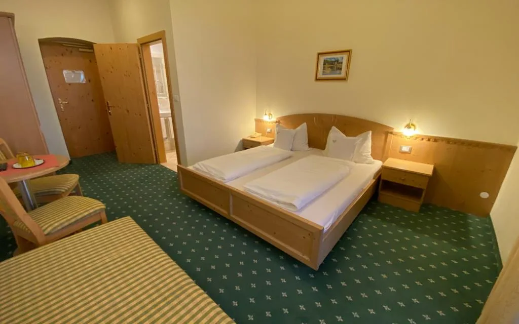 Camera spaziosa con moquette verde, letto matrimoniale in legno e zona bagno adiacente