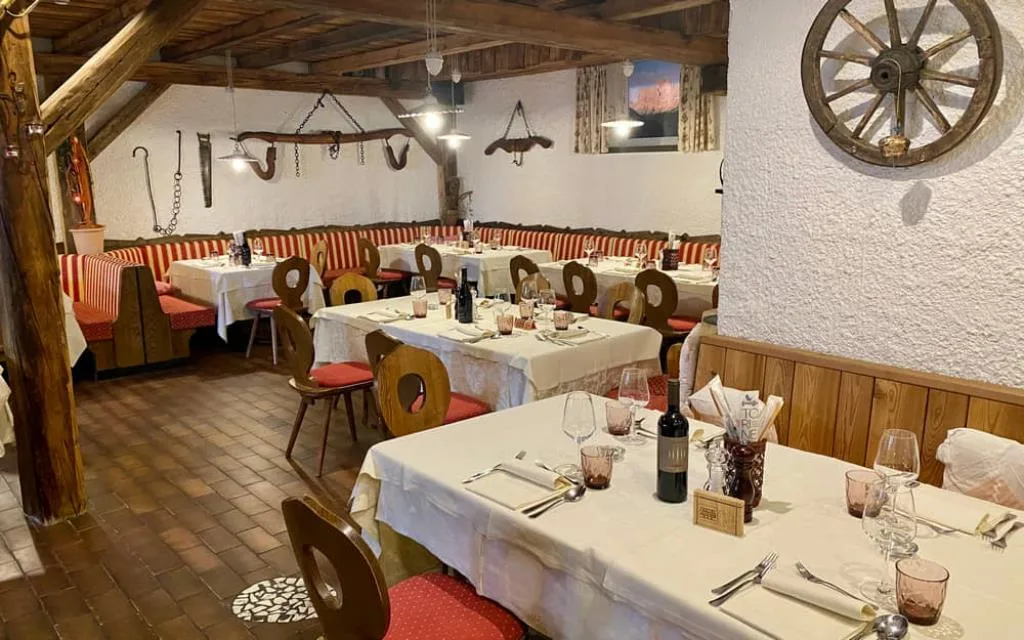 Sala ristorante rustica con travi in legno, tavoli apparecchiati e ruota di carro sul muro