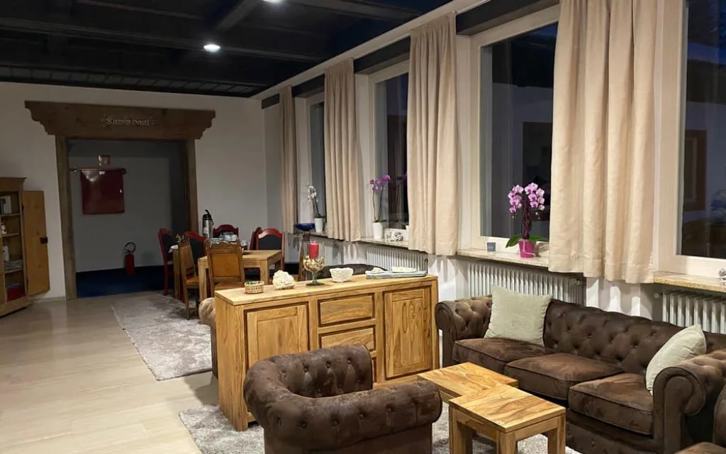 Salotto con poltrone e divani in pelle marrone, credenza in legno e grandi finestre