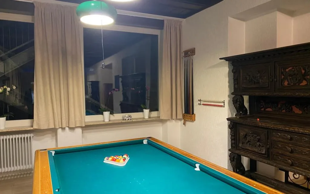 Sala giochi con tavolo da biliardo, credenza intagliata in legno e finestre