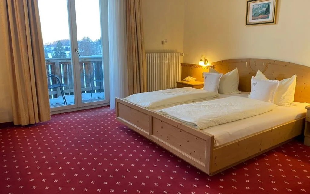 Camera con letto matrimoniale in legno, moquette rossa e porta finestra sul balcone innevato