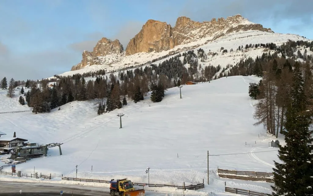 Pista da sci innevata con impianto di risalita e vetta dolomitica illuminata dal sole