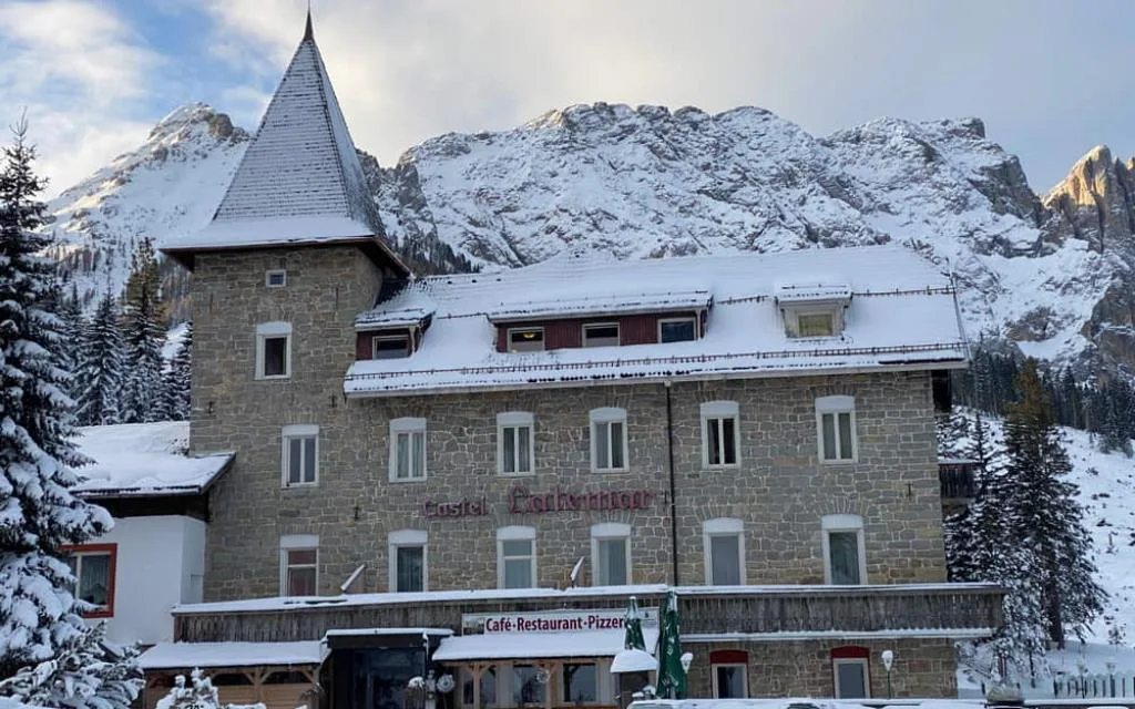 Facciata dell'hotel in pietra sotto la neve con montagne dolomitiche sullo sfondo