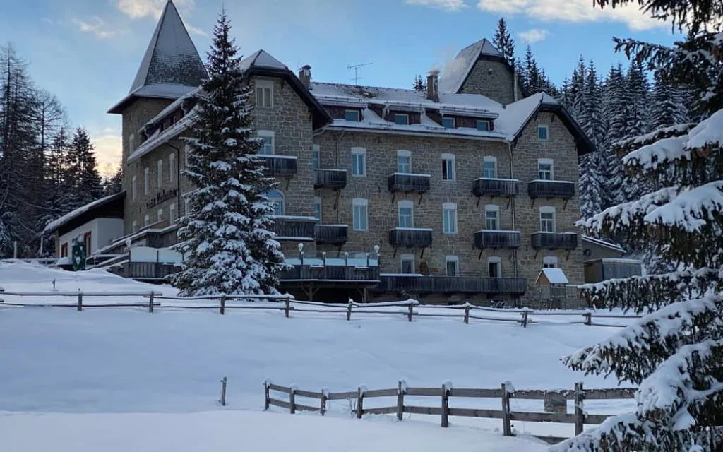 Vista posteriore dell'hotel innevato con torretta, balconi e abeti carichi di neve