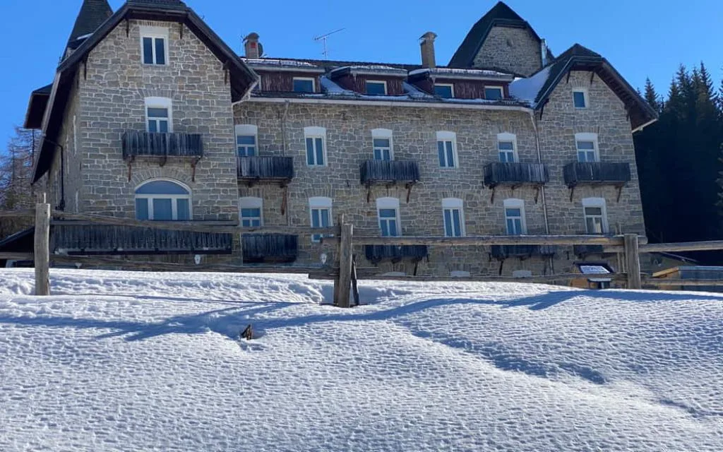Facciata storica dell'hotel in pietra con balconi in legno e prato innevato in primo piano