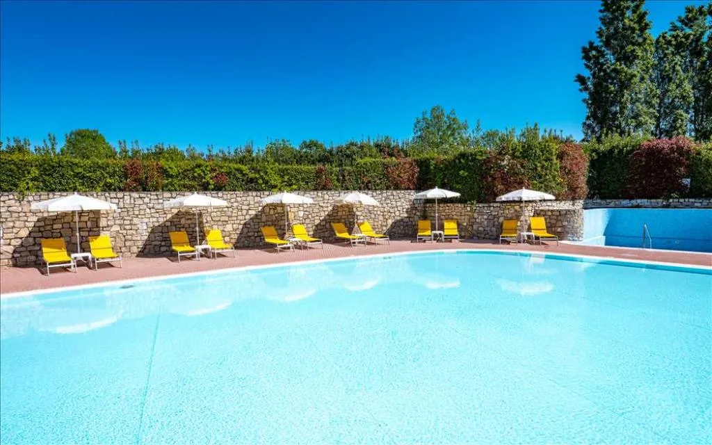Piscina esterna con lettini gialli e ombrelloni lungo un muro in pietra