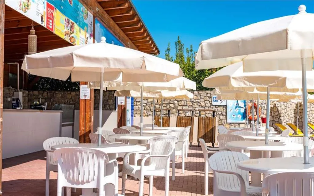 Bar esterno con tavoli e sedie bianche sotto ombrelloni vicino alla piscina