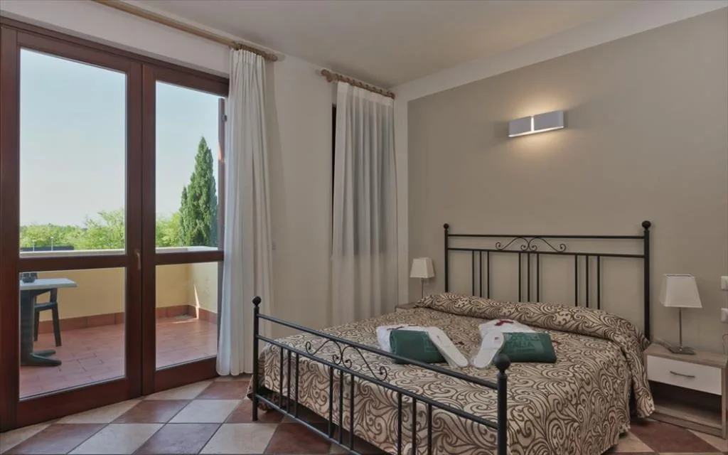 Camera matrimoniale con letto in ferro battuto, uscita sul balcone e vista sul verde