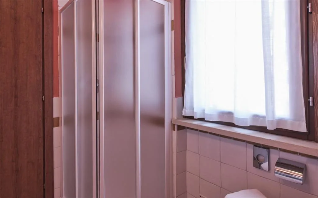 Bagno con doccia a soffietto e finestra con tende bianche