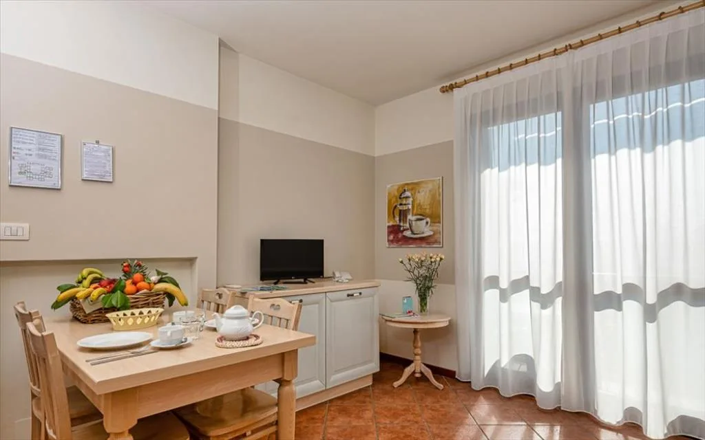 Zona pranzo luminosa con tavolo in legno, TV e ampia finestra