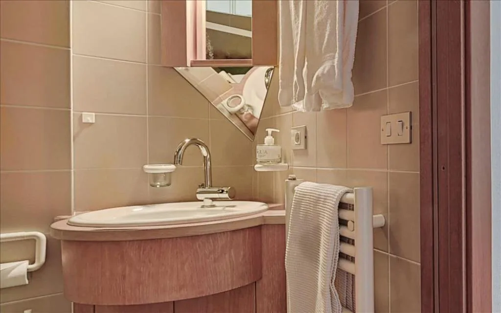 Bagno con lavabo curvo, specchio angolare e piastrelle beige