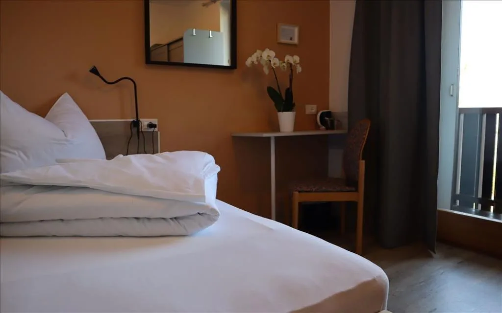 Dettaglio di camera con letto bianco, orchidea, scrivania e parete arancione