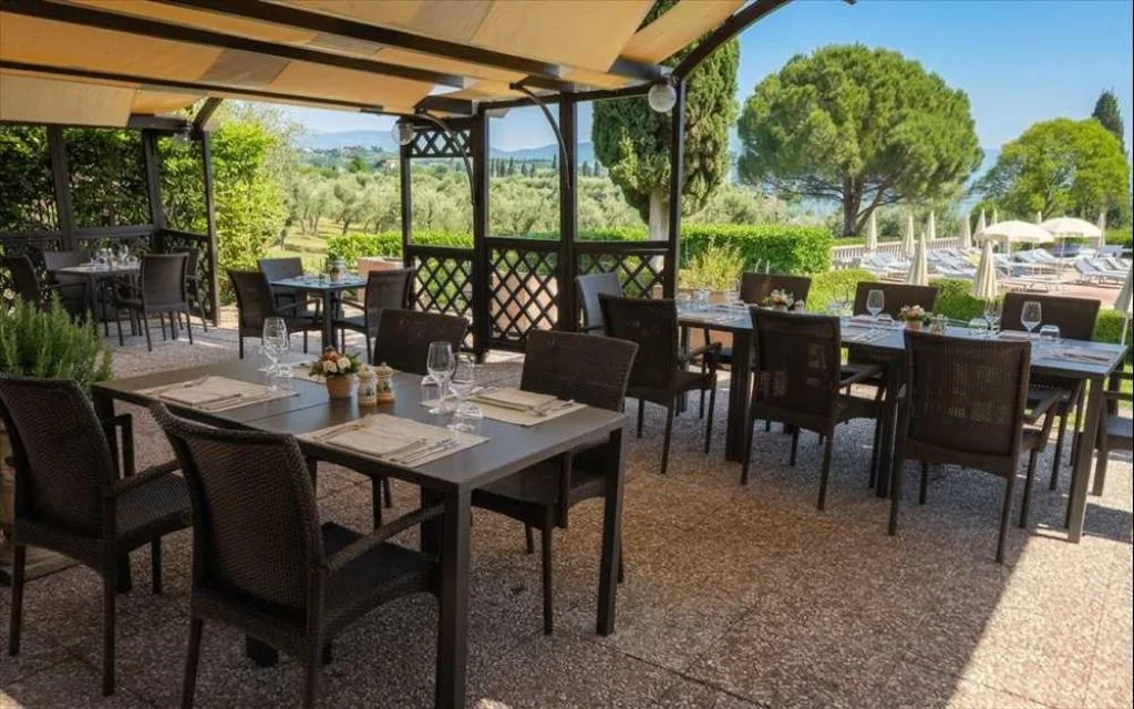Ristorante all'aperto sotto pergolato con tavoli apparecchiati e vista sul verde