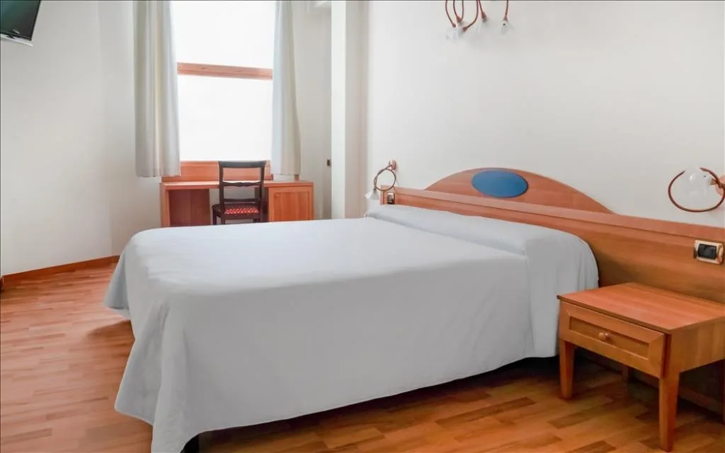 Camera con letto matrimoniale, scrivania e finestra con tende bianche