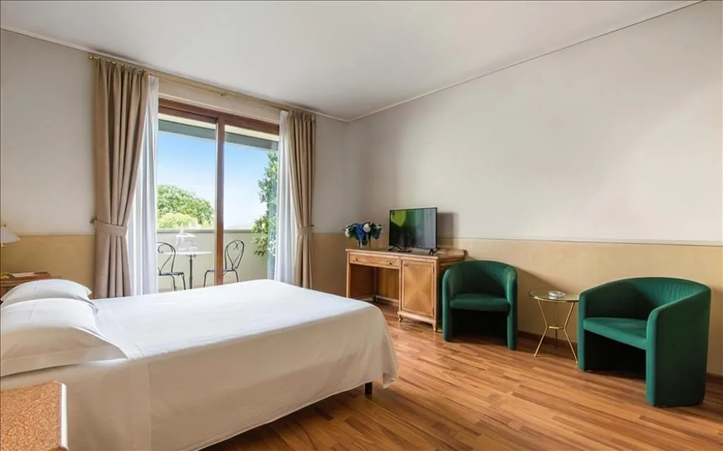 Camera luminosa con letto, poltrone verdi, TV e balcone con vista