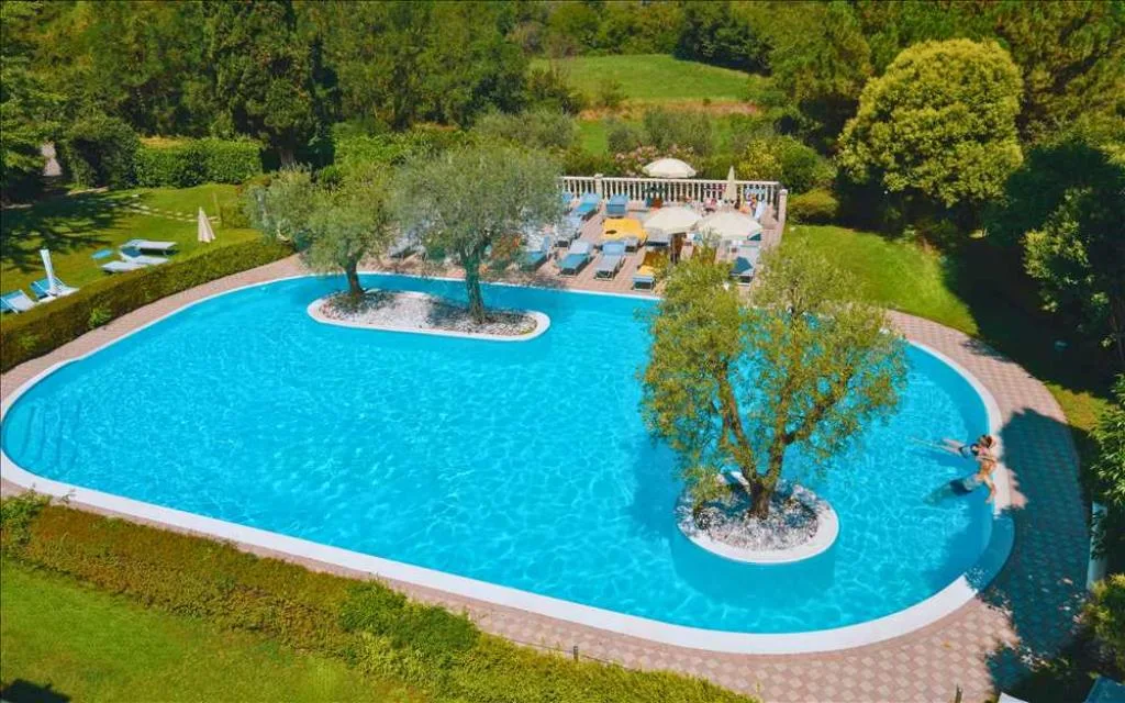 Veduta aerea della piscina con isole di ulivi e area lettini circondata dal verde