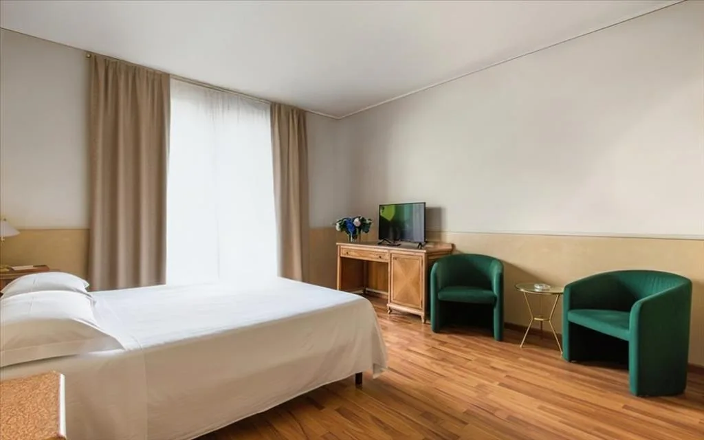 Camera spaziosa con letto matrimoniale, poltrone verdi e TV