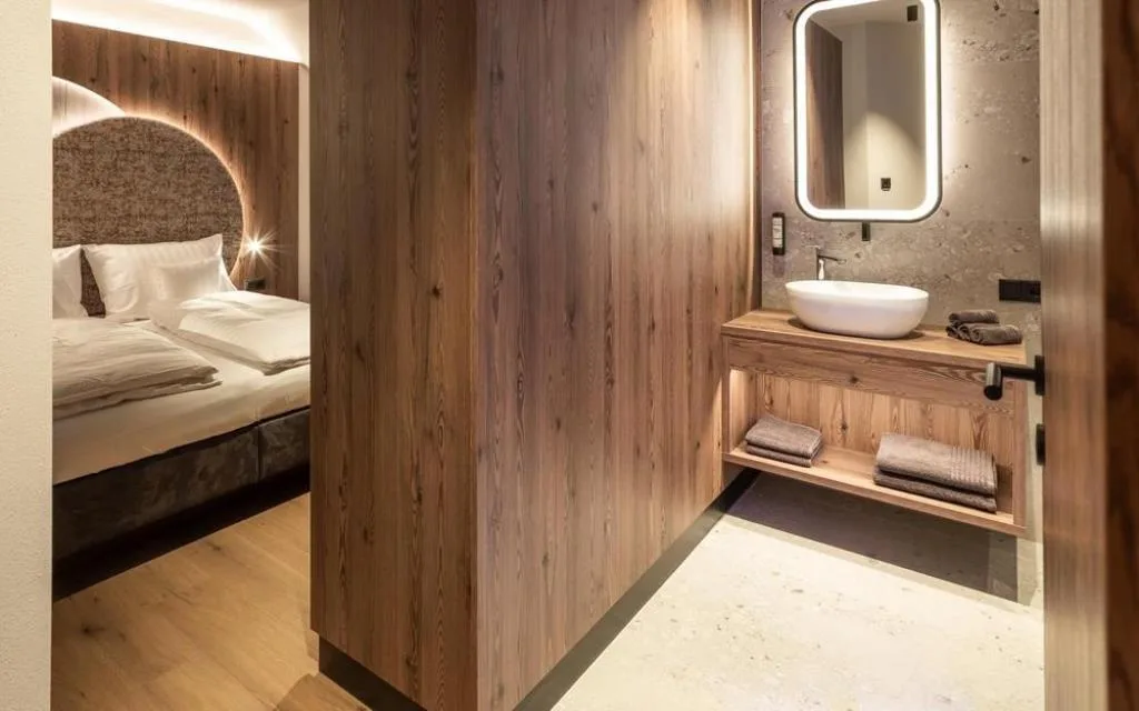 Bagno con lavabo tondo in legno e specchio illuminato accanto alla camera