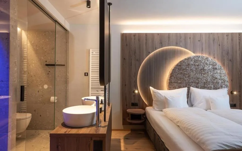 Camera con letto matrimoniale e bagno open space con doccia in vetro e lavabo