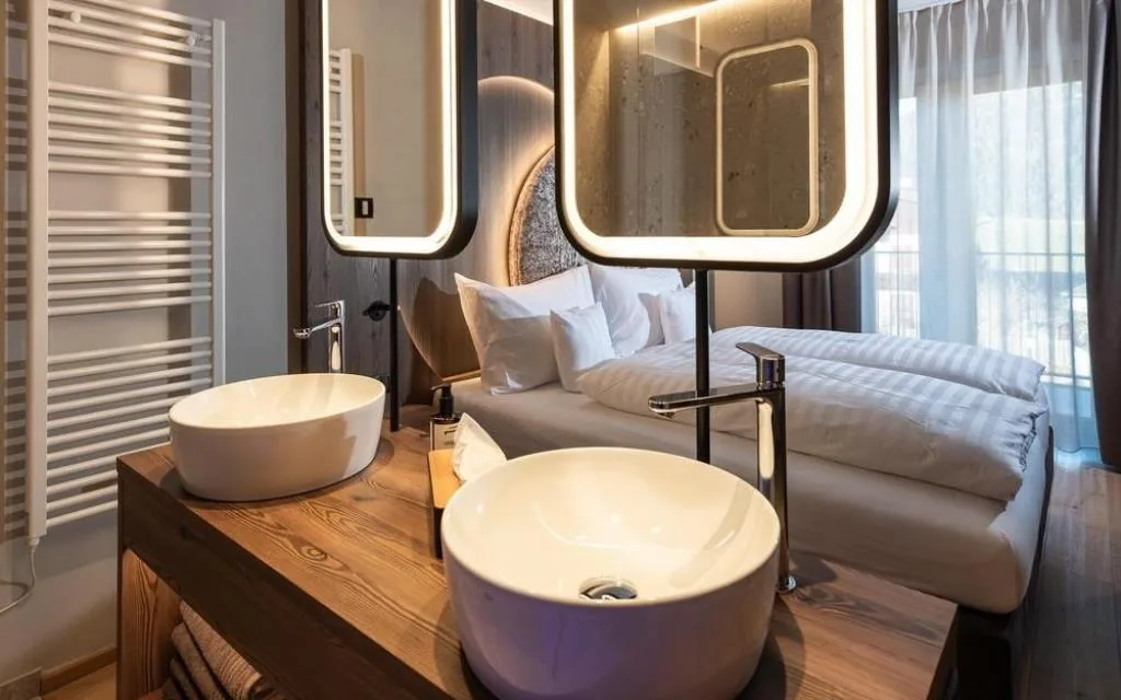 Doppio lavabo tondo con specchi illuminati e vista sul letto della camera