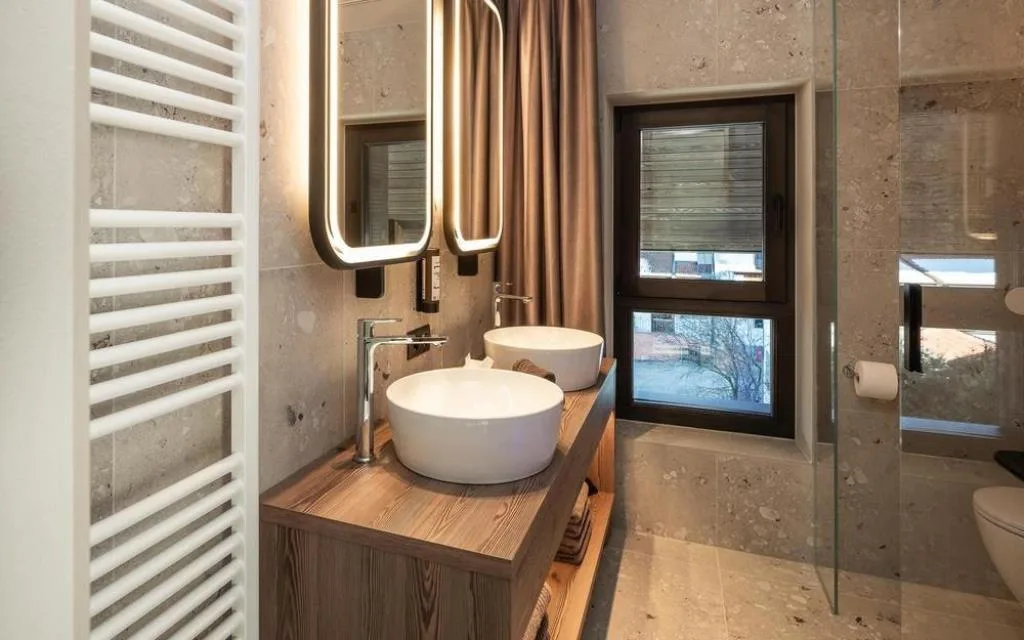 Bagno in pietra con doppio lavabo, doccia in vetro e finestra con vista