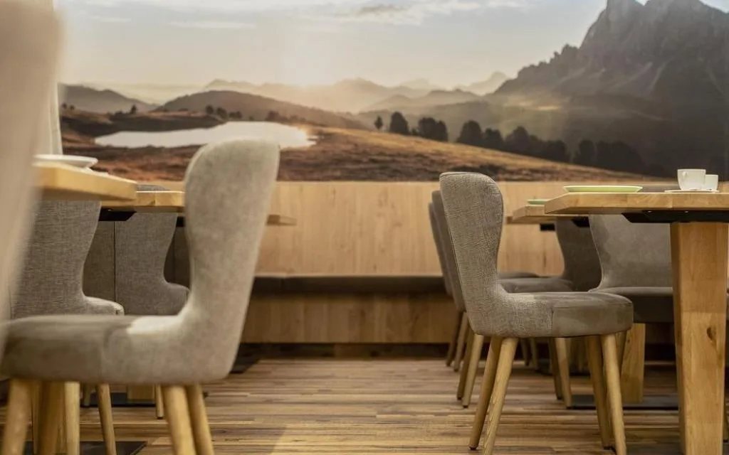 Sala colazione con sedie imbottite grigie, tavoli in legno e murale di paesaggio montano
