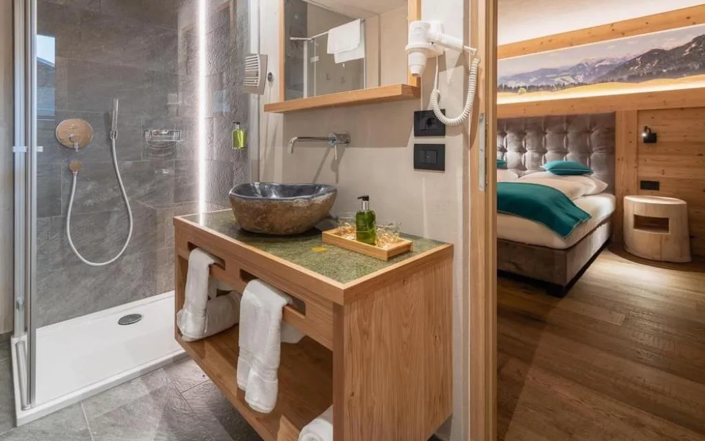 Bagno moderno con doccia, lavabo in pietra e mobile in legno con vista sulla camera