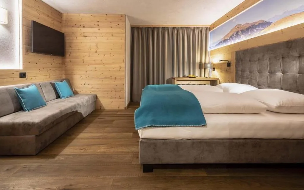 Camera con letto matrimoniale, divano grigio e TV a parete in ambiente in legno