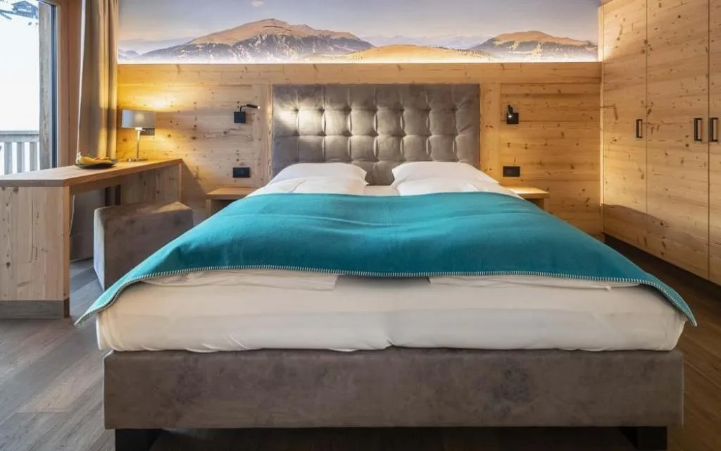 Letto matrimoniale con coperta turchese e murale di paesaggio montano illuminato