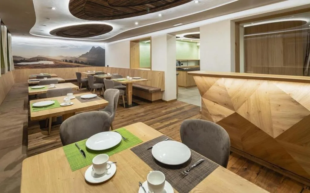 Sala ristorante con tavoli apparecchiati, sedie grigie e murale di paesaggio alpino