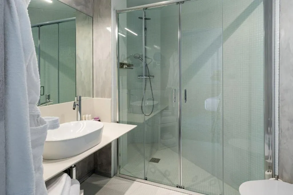 Bagno moderno con doccia in vetro, lavabo bianco e parete a specchio