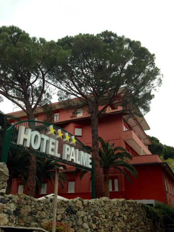 Facciata rosa dell'Hotel Palme con insegna tra alberi e palme