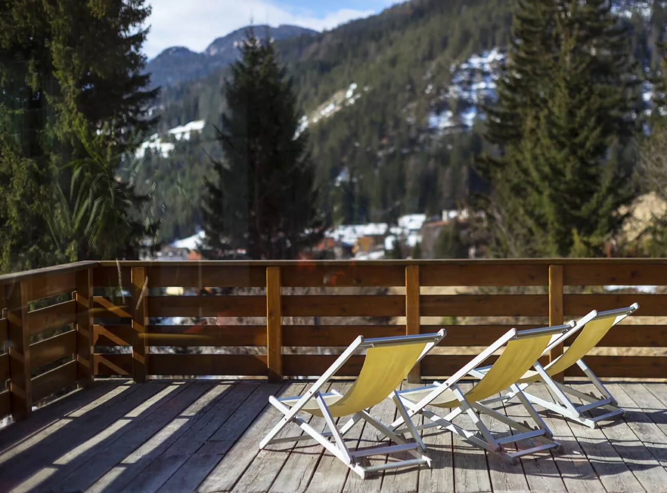 Terrazza in legno con sdraio gialle e vista sui boschi e le montagne