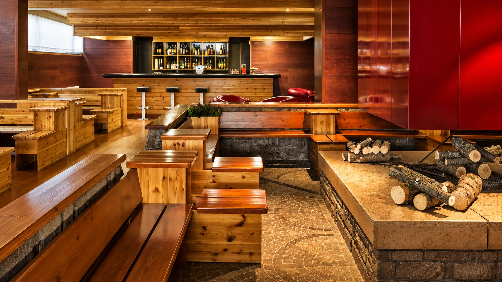 Bar interno con sedute in legno, bancone e caminetto con legna