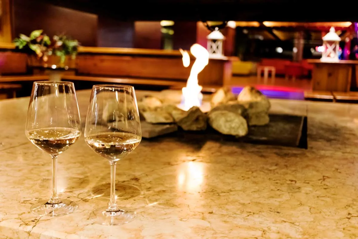 Due calici di vino bianco su tavolo con caminetto a vista sullo sfondo