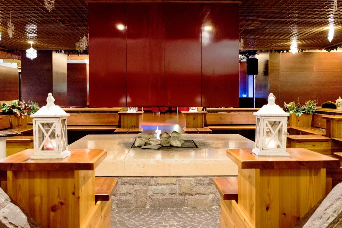 Area lounge con focolare centrale, lanterne bianche e sedute in legno