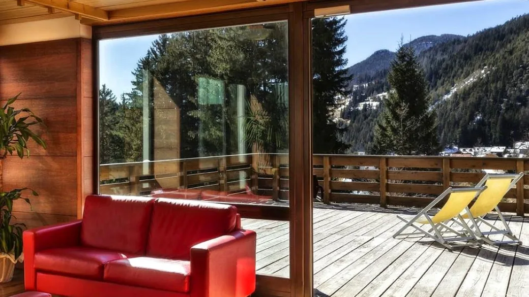 Area relax interna con divano rosso e terrazza con vista sulle montagne