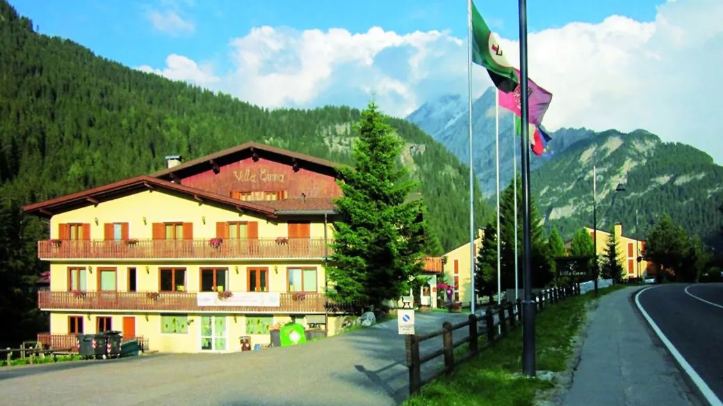 Hotel Villa Emma in estate con bandiere e montagne boscose sullo sfondo