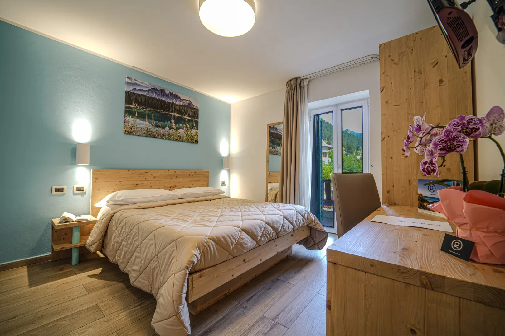 Camera matrimoniale con parete verde acqua, letto in legno e vista sulle montagne dalla finestra