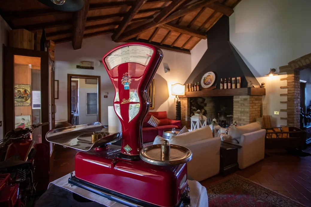 Salotto rustico con bilancia d'epoca rossa, camino in mattoni e divani